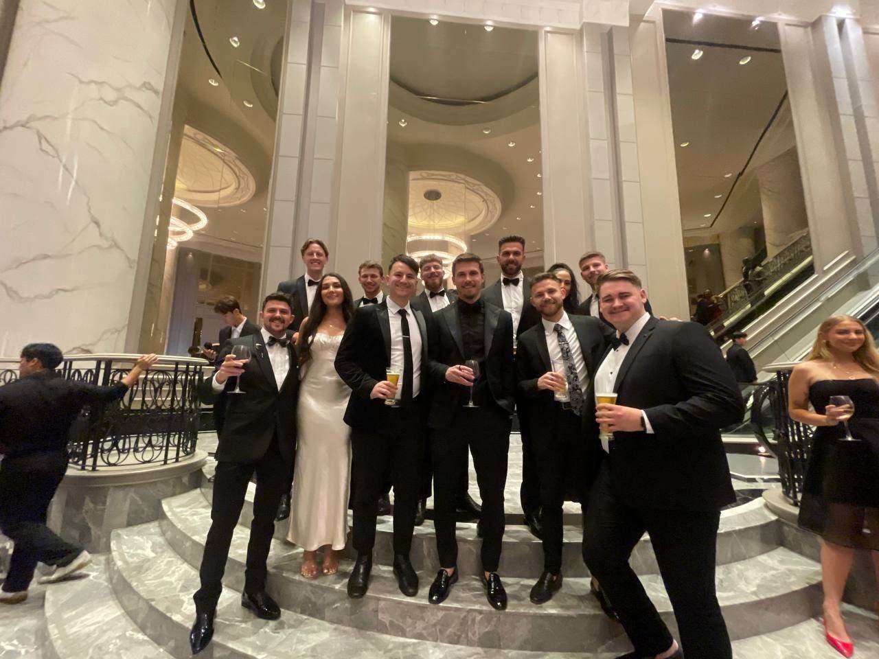 Team dressed in black tie on a grand hotel staircase in Malaysia